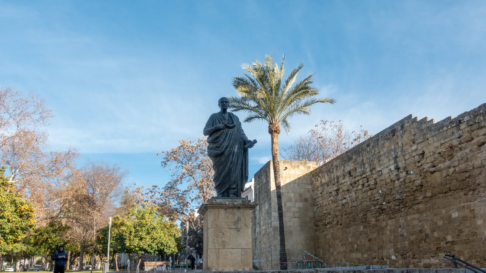 Modern bronze standing statue of Seneca beside the medieval Puerta de Almodovar gate in Cordoba.